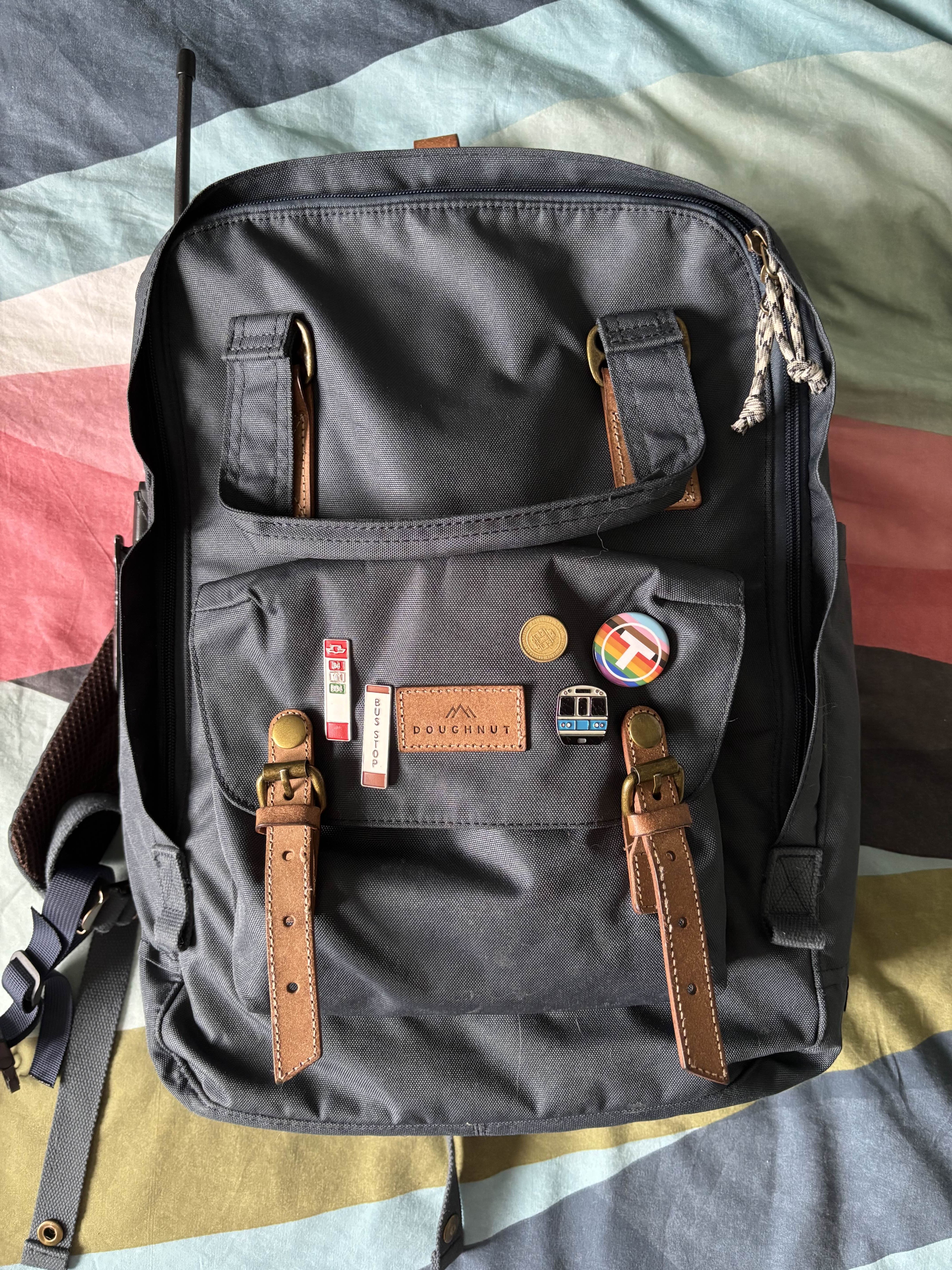 Photo of the front of the Donut Macaroon Backpack. Visible are pins of Toronto Transit Commission bus stops, an MBTA token pin, an MBTA pride pin and an MBTA blue line pin