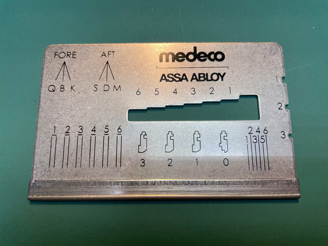 Photo of a Medeco M4 decoder card. The card includes a punched out section in a stairshep shape. Each step on the stairshep represents a possible depth that a key could be at. Additionally there are measurement tools for the M3 sidebar depth on the left side and on the right side measurements for fore and aft position. There are additional diagrams for determining the cut angle notation and side-bitting pins diagrams for M4.